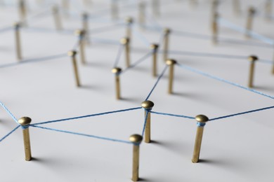 Photo of Network connection. Nails linked together by thread on white table, closeup