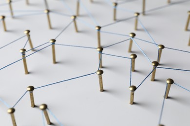 Photo of Network connection. Nails linked together by thread on white table, closeup