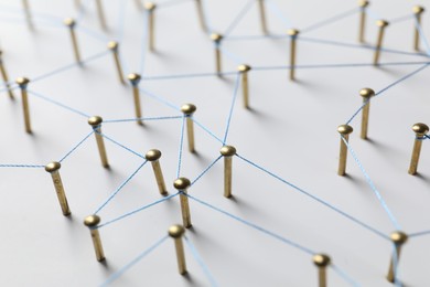 Photo of Network connection. Nails linked together by thread on white table, closeup