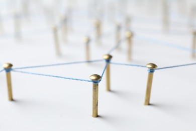 Network connection. Nails linked together by thread on white table, closeup