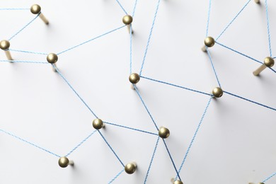 Photo of Network connection. Nails linked together by thread on white table, top view