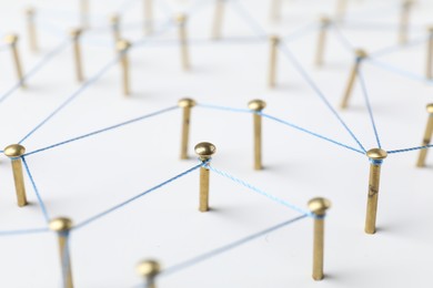 Photo of Network connection. Nails linked together by thread on white table, closeup