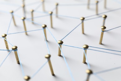 Photo of Network connection. Nails linked together by thread on white table, closeup