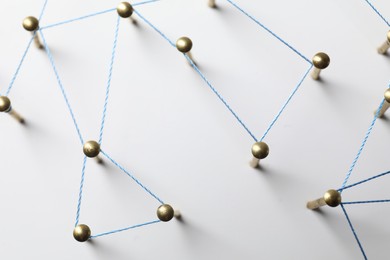 Photo of Network connection. Nails linked together by thread on white table, top view