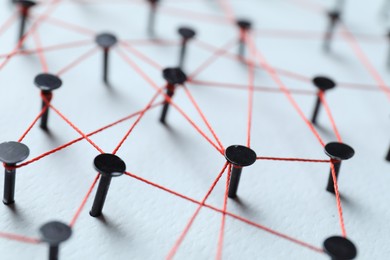 Photo of Network connection. Nails linked together by thread on white table, closeup