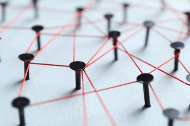 Photo of Network connection. Nails linked together by thread on white table, closeup