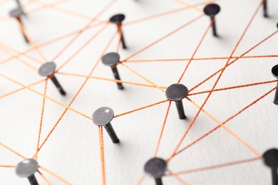 Photo of Network connection. Nails linked together by thread on white table, closeup