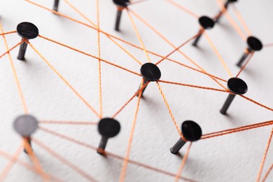 Photo of Network connection. Nails linked together by thread on white table, closeup