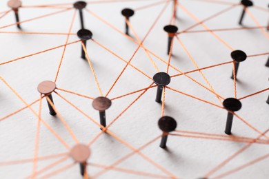 Photo of Network connection. Nails linked together by thread on white table, closeup