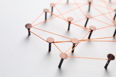 Photo of Network connection. Nails linked together by thread on white table, closeup. Space for text