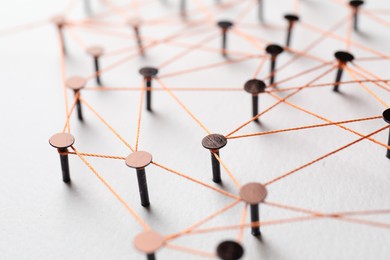 Photo of Network connection. Nails linked together by thread on white table, closeup