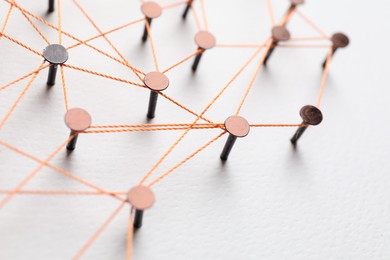 Photo of Network connection. Nails linked together by thread on white table, closeup