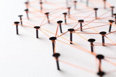 Photo of Network connection. Nails linked together by thread on white table, closeup