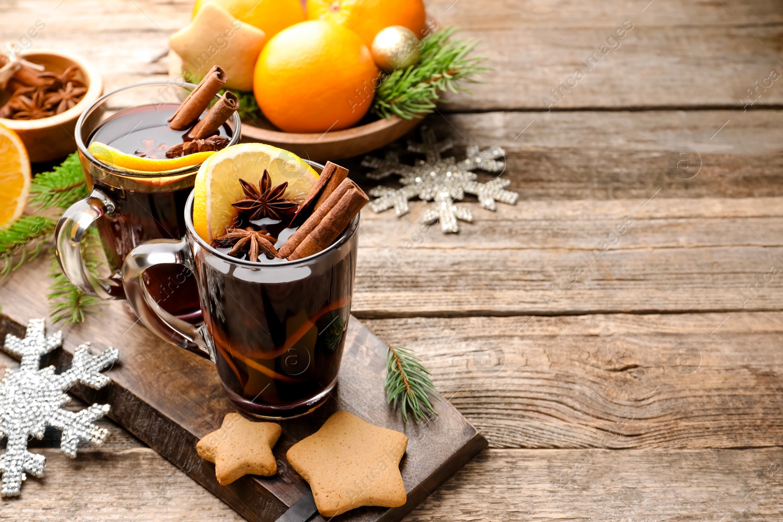 Photo of Tasty mulled wine with spices, orange slices, cookies and Christmas decor on wooden table. Space for text