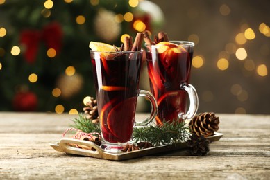 Photo of Tasty mulled wine with spices and decor on wooden table against blurred Christmas lights, bokeh effect