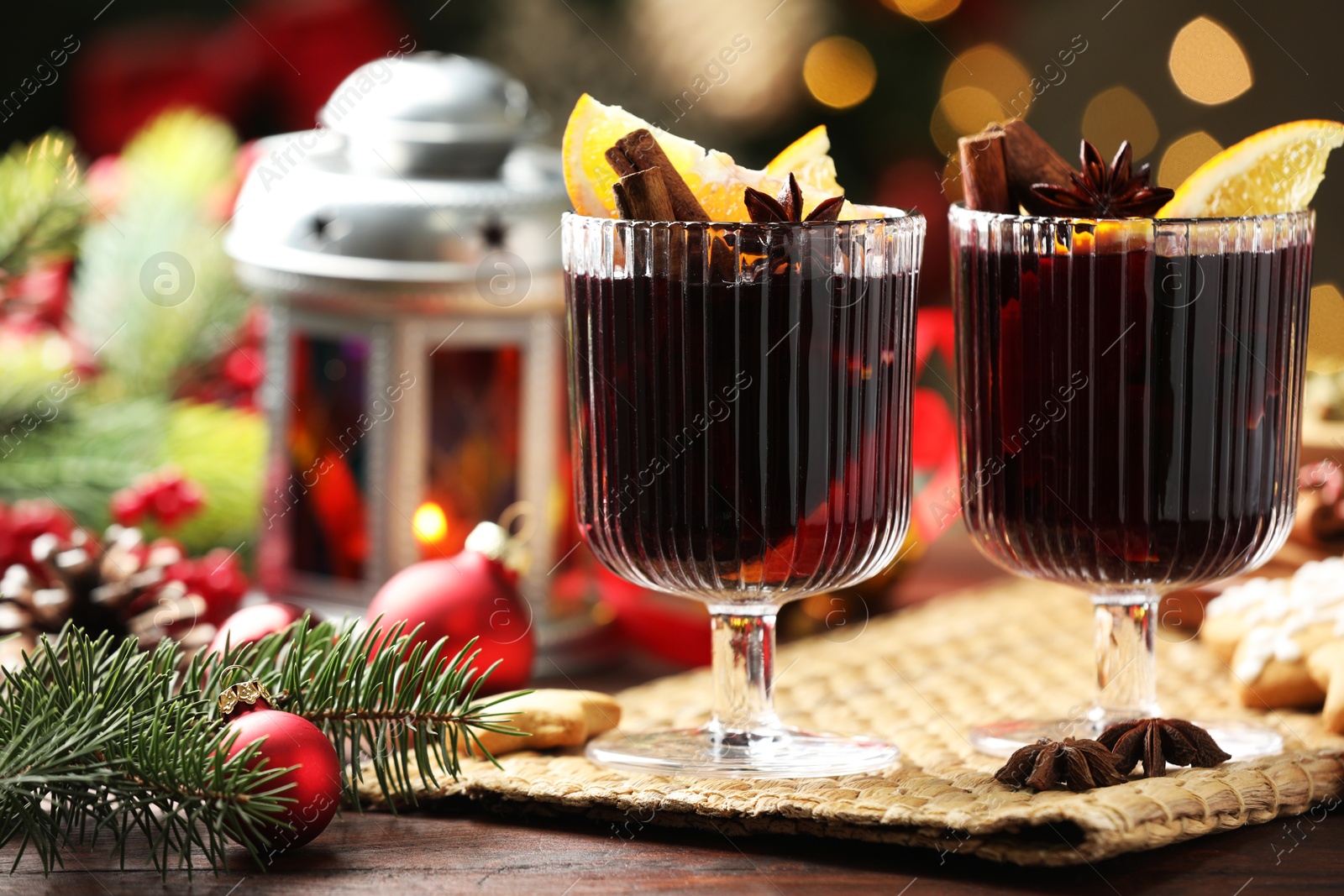 Photo of Tasty mulled wine with spices and decor on wooden table against blurred Christmas lights, closeup. Bokeh effect