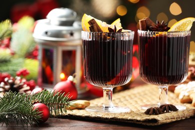 Photo of Tasty mulled wine with spices and decor on wooden table against blurred Christmas lights, closeup. Bokeh effect