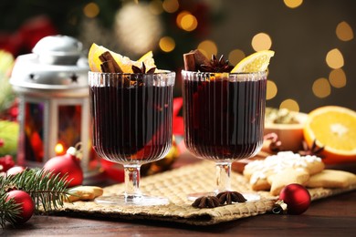 Photo of Tasty mulled wine with spices, cookies and decor on wooden table against blurred Christmas lights, bokeh effect