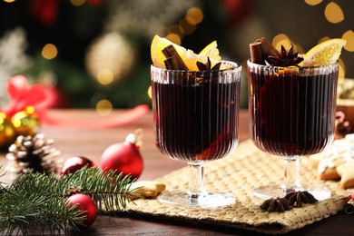 Photo of Tasty mulled wine with spices and decor on wooden table against blurred Christmas lights, closeup. Bokeh effect