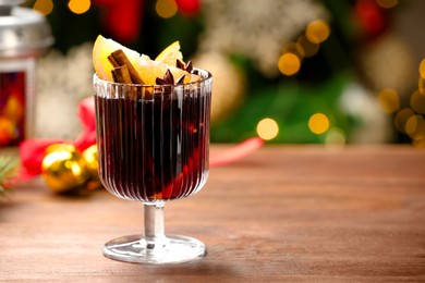 Photo of Tasty mulled wine with spices on wooden table against blurred Christmas lights, space for text. Bokeh effect