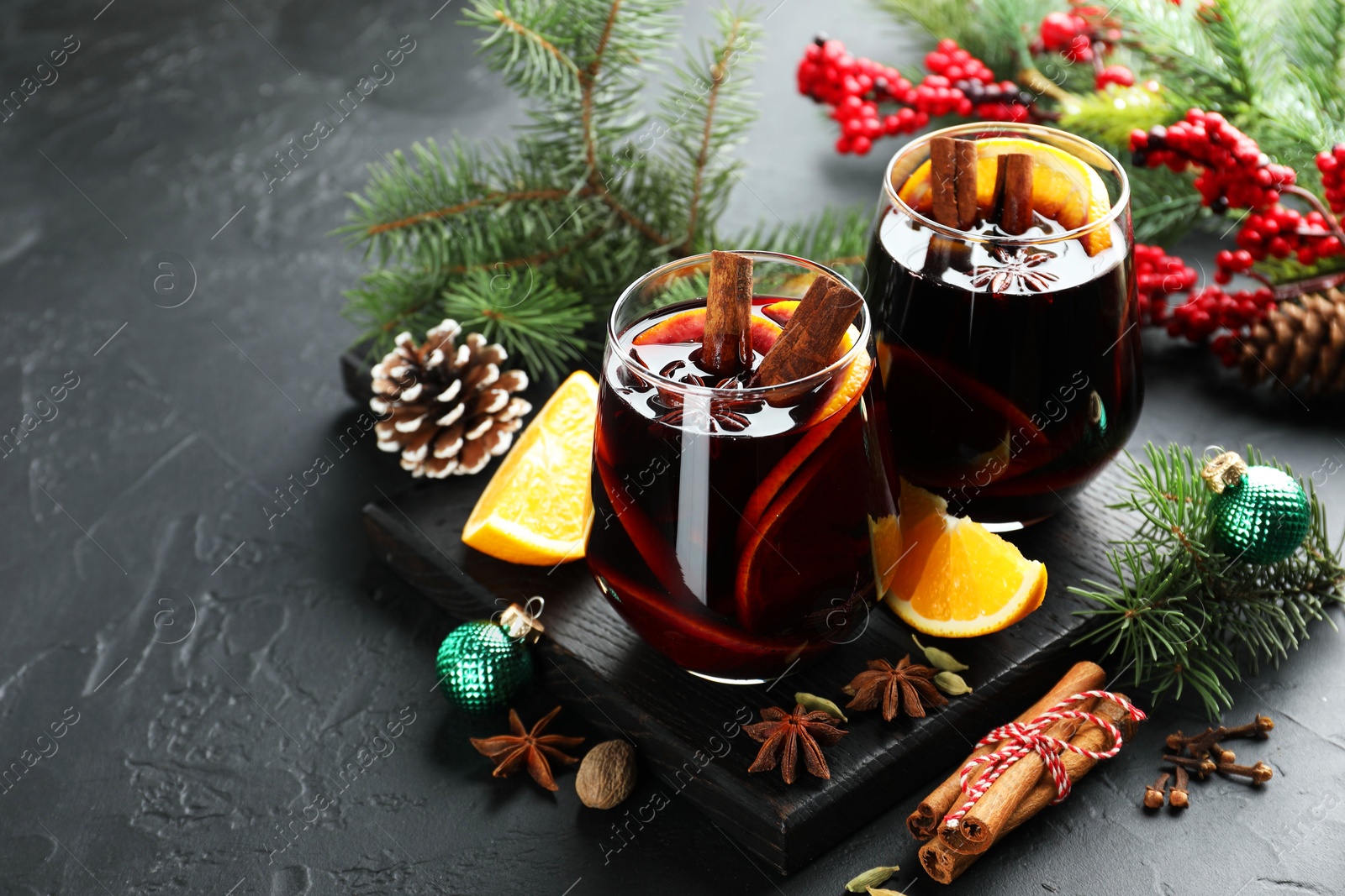 Photo of Tasty mulled wine with spices and Christmas decor on black table, space for text