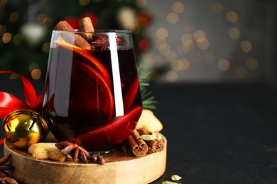 Photo of Tasty mulled wine with spices, cookies and Christmas decor on black table, closeup. Bokeh effect