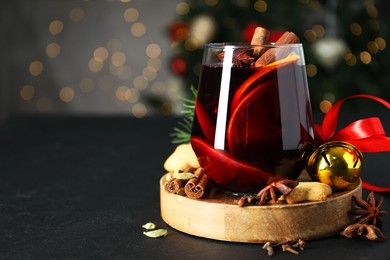 Photo of Tasty mulled wine with spices, cookies and Christmas decor on black table, closeup. Bokeh effect