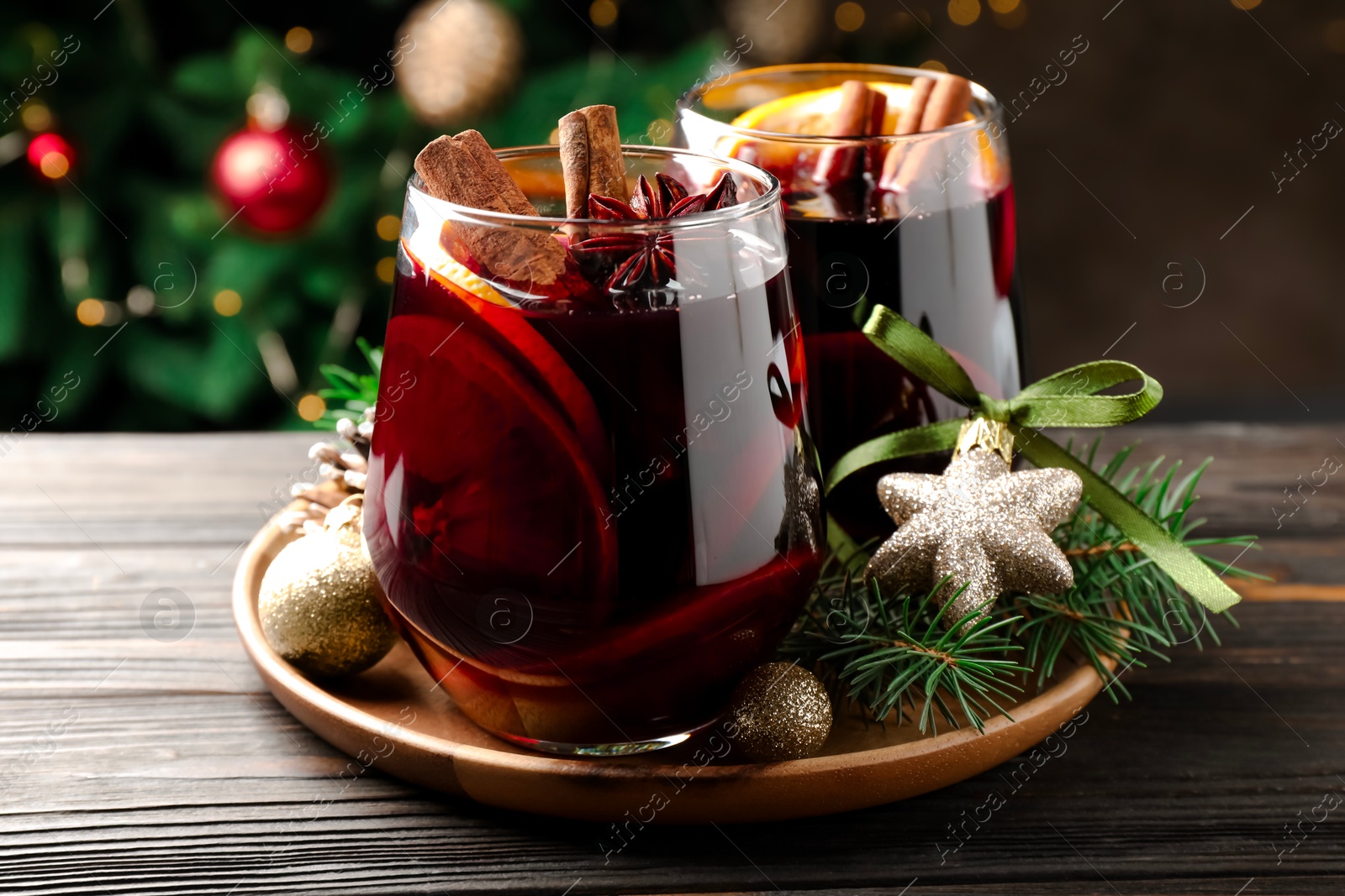 Photo of Tasty mulled wine with spices and Christmas decor on wooden table, closeup