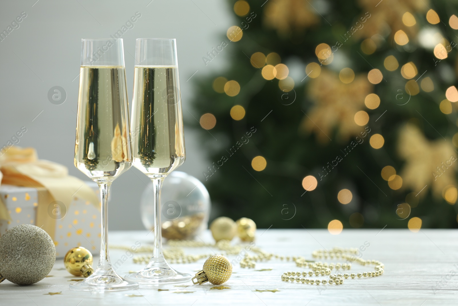 Photo of Champagne in glasses and Christmas decor on white wooden table against blurred lights, space for text. Bokeh effect