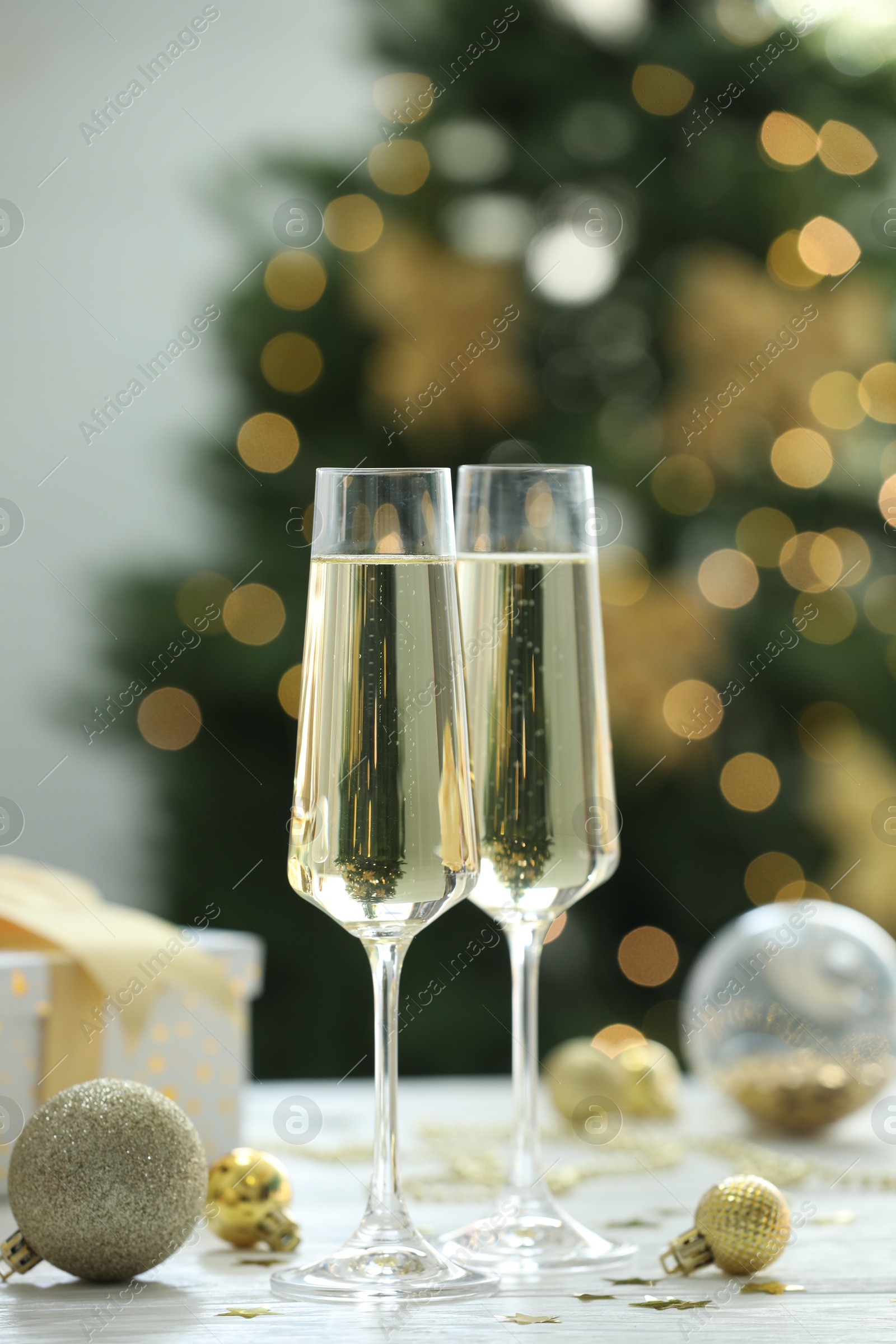 Photo of Champagne in glasses and Christmas decor on white wooden table against blurred lights. Bokeh effect