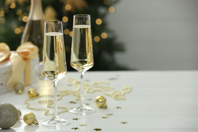 Photo of Champagne in glasses and Christmas decor on white wooden table against blurred lights, space for text. Bokeh effect