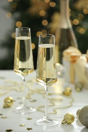 Photo of Champagne in glasses and Christmas decor on white wooden table against blurred lights. Bokeh effect