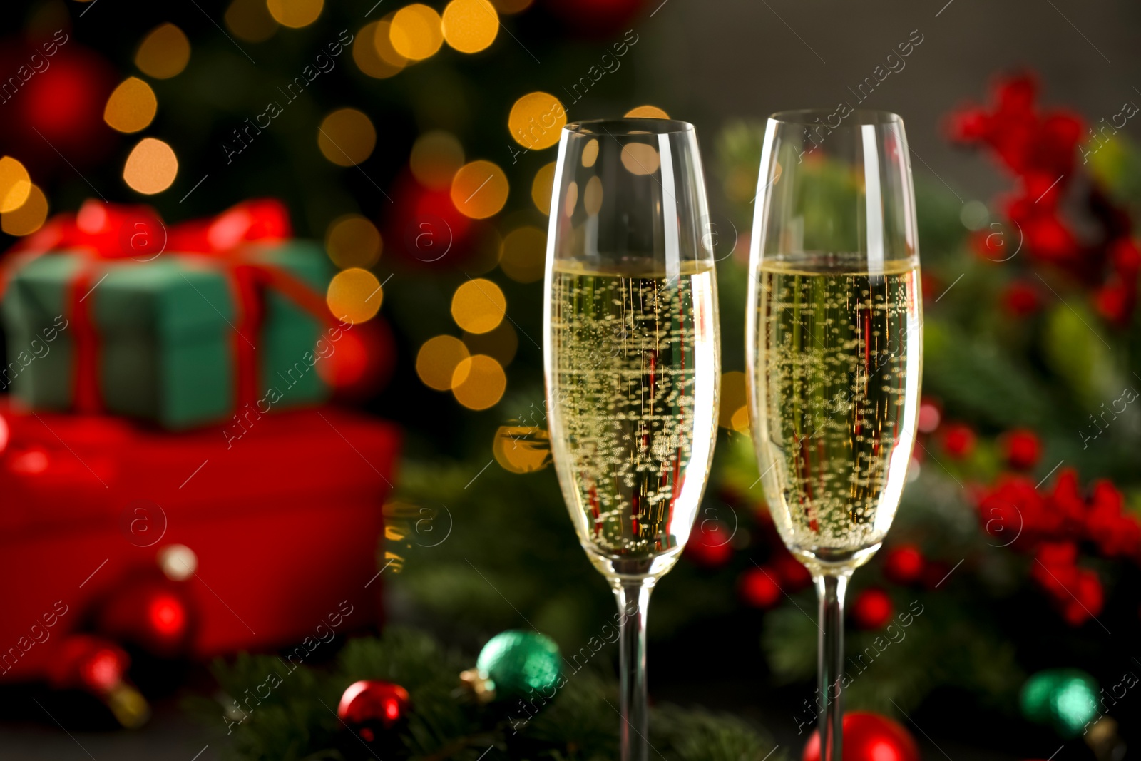 Photo of Champagne in glasses with decor against blurred Christmas lights, closeup and space for text