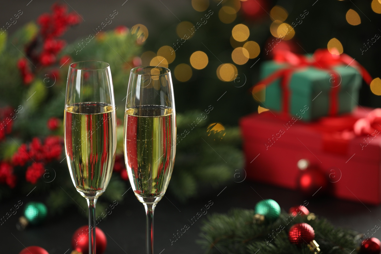 Photo of Champagne in glasses with decor against blurred Christmas lights, closeup and space for text