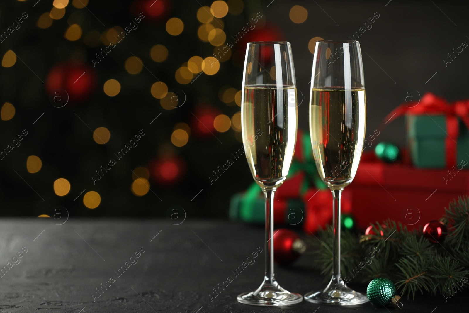 Photo of Champagne in glasses and decor on black table against blurred Christmas lights, space for text