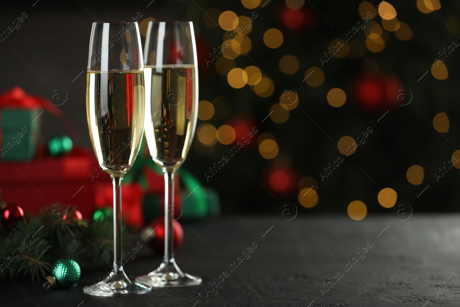 Photo of Champagne in glasses and decor on black table against blurred Christmas lights, space for text