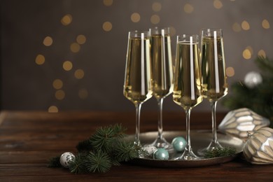 Photo of Champagne in glasses and decor on wooden table against blurred Christmas lights, space for text. Bokeh effect