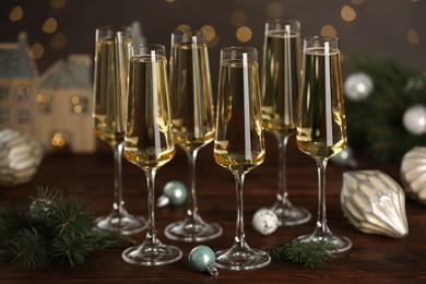 Photo of Champagne in glasses and Christmas decor on wooden table against blurred lights. Bokeh effect