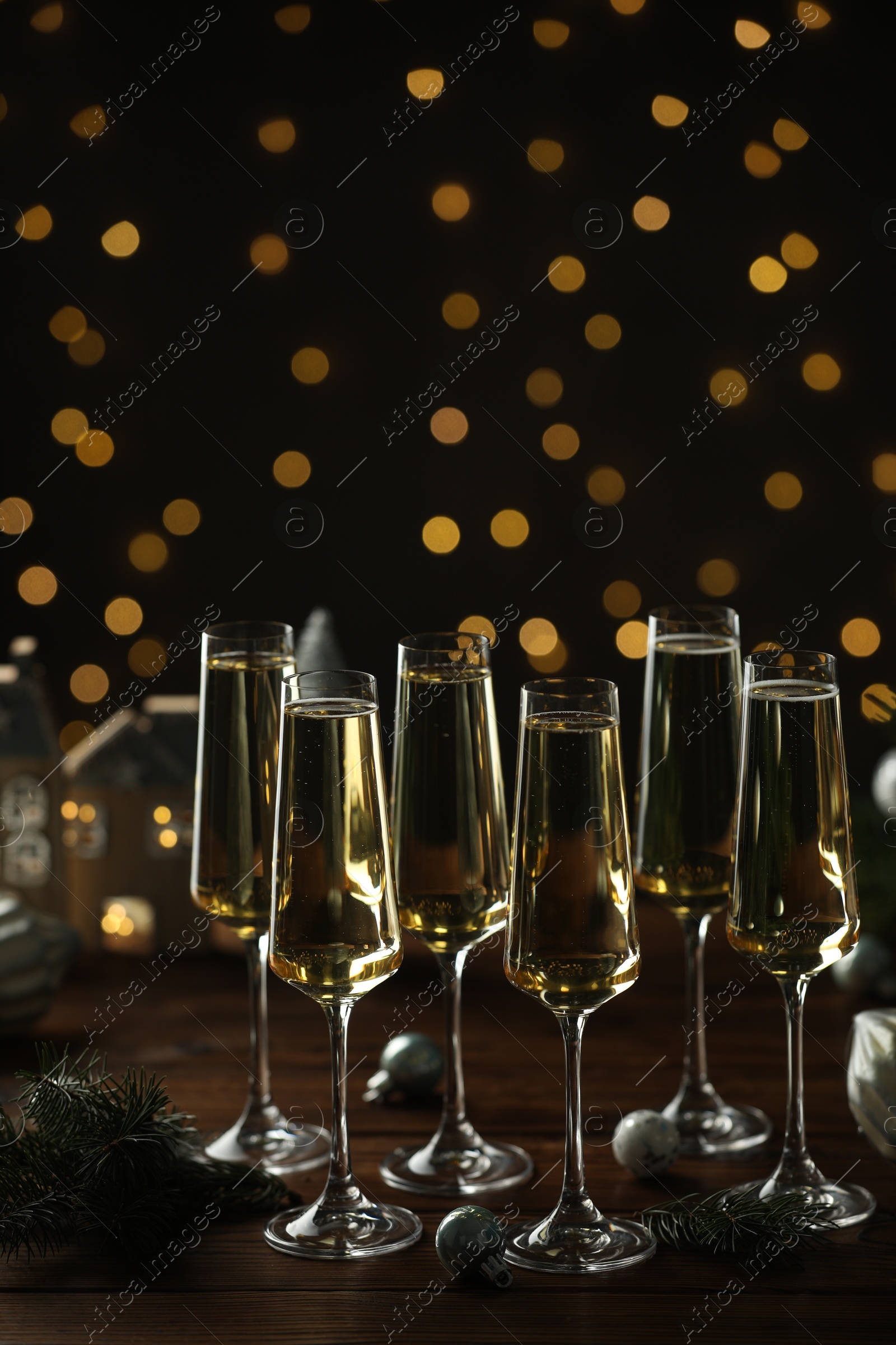 Photo of Champagne in glasses and decor on wooden table against blurred Christmas lights. Bokeh effect