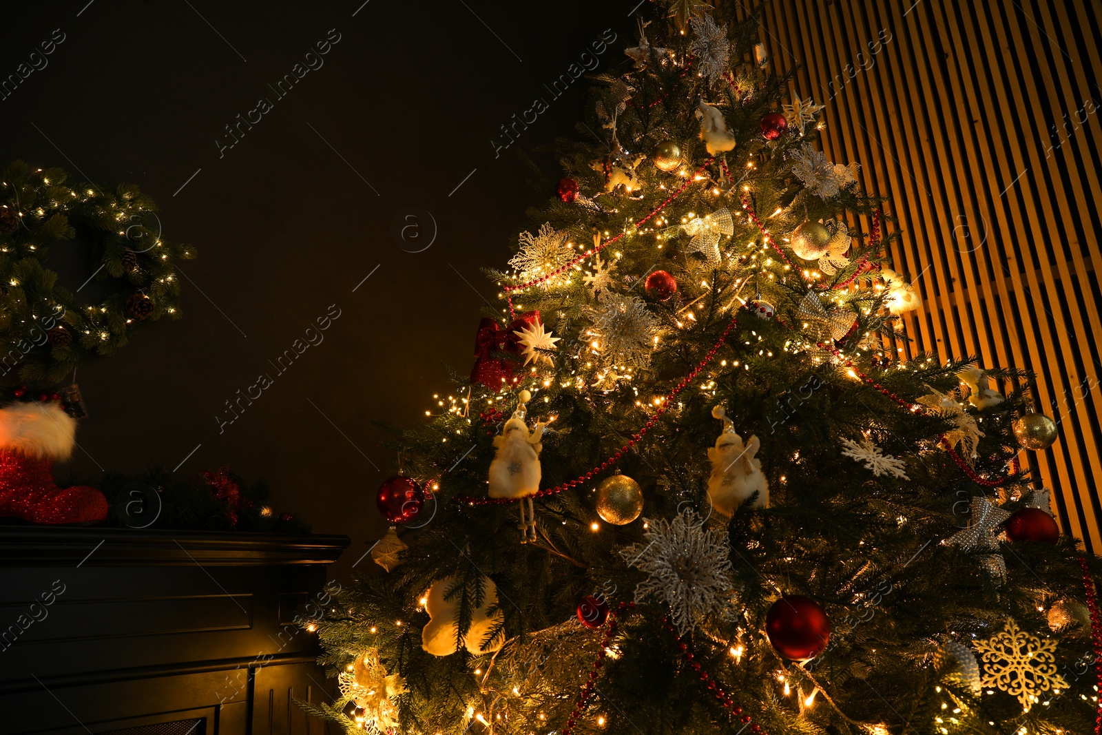 Photo of Christmas tree with festive decor in dark room, low angle view