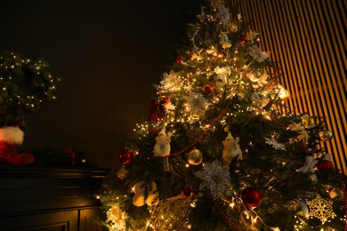 Photo of Christmas tree with festive decor in dark room, low angle view