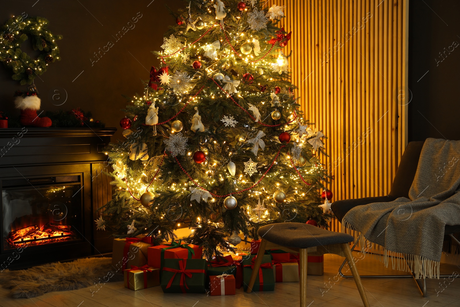 Photo of Christmas tree with festive decor, presents, fireplace and armchair in cozy room