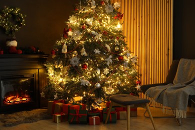 Photo of Christmas tree with festive decor, presents, fireplace and armchair in cozy room