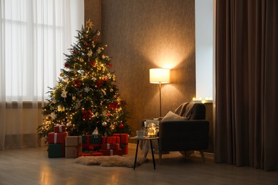 Photo of Christmas tree with festive decor, presents, coffee table and armchair in cozy room