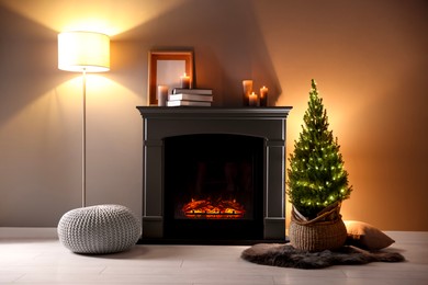 Photo of Small spruce tree in basket decorated with Christmas lights near fireplace indoors