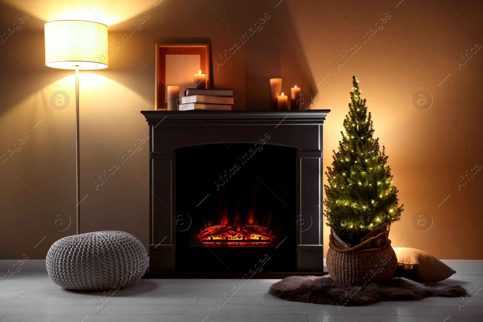 Photo of Small spruce tree in basket decorated with Christmas lights near fireplace indoors