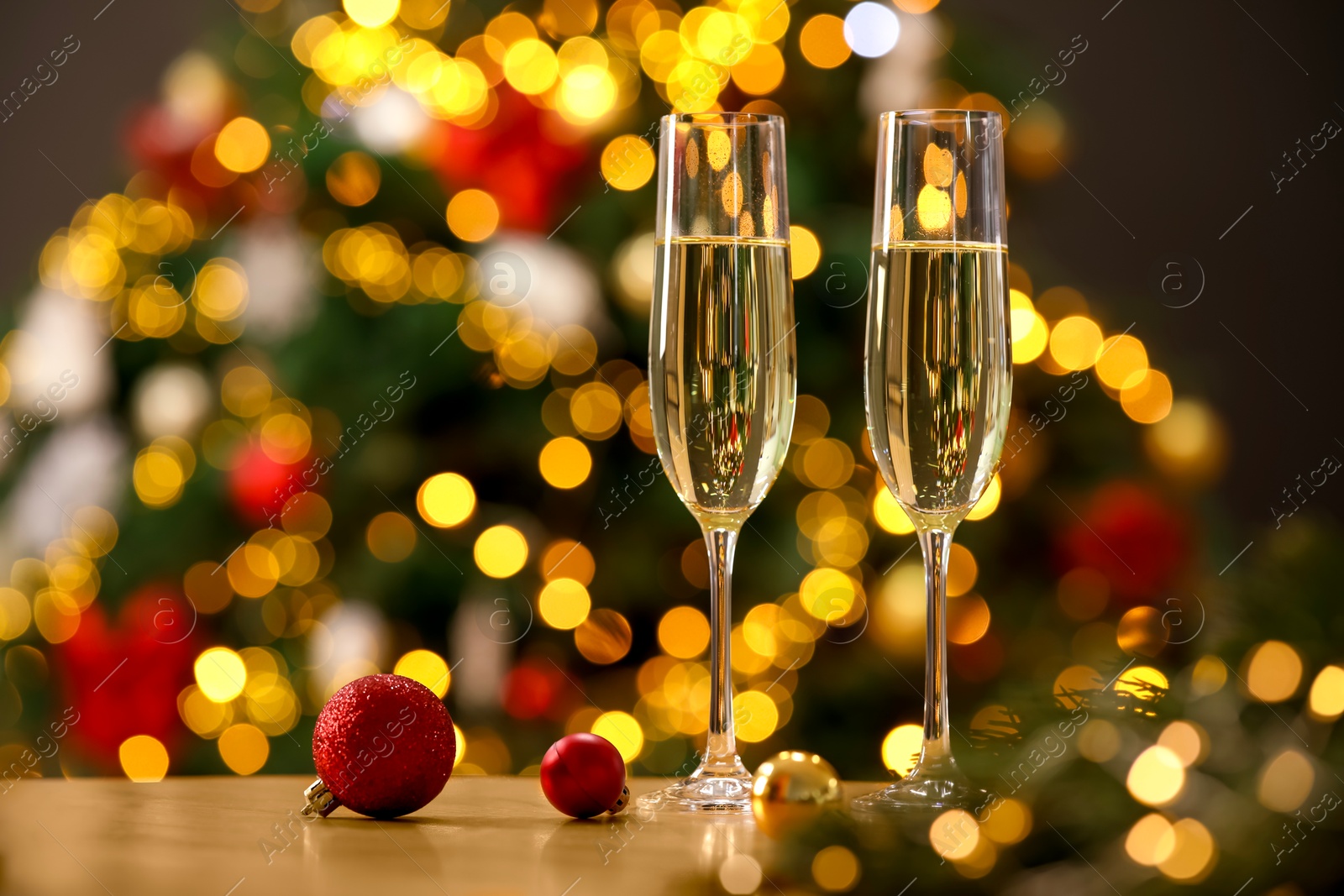 Photo of Champagne in glasses and festive ornaments on wooden table against blurred Christmas lights, space for text. Bokeh effect