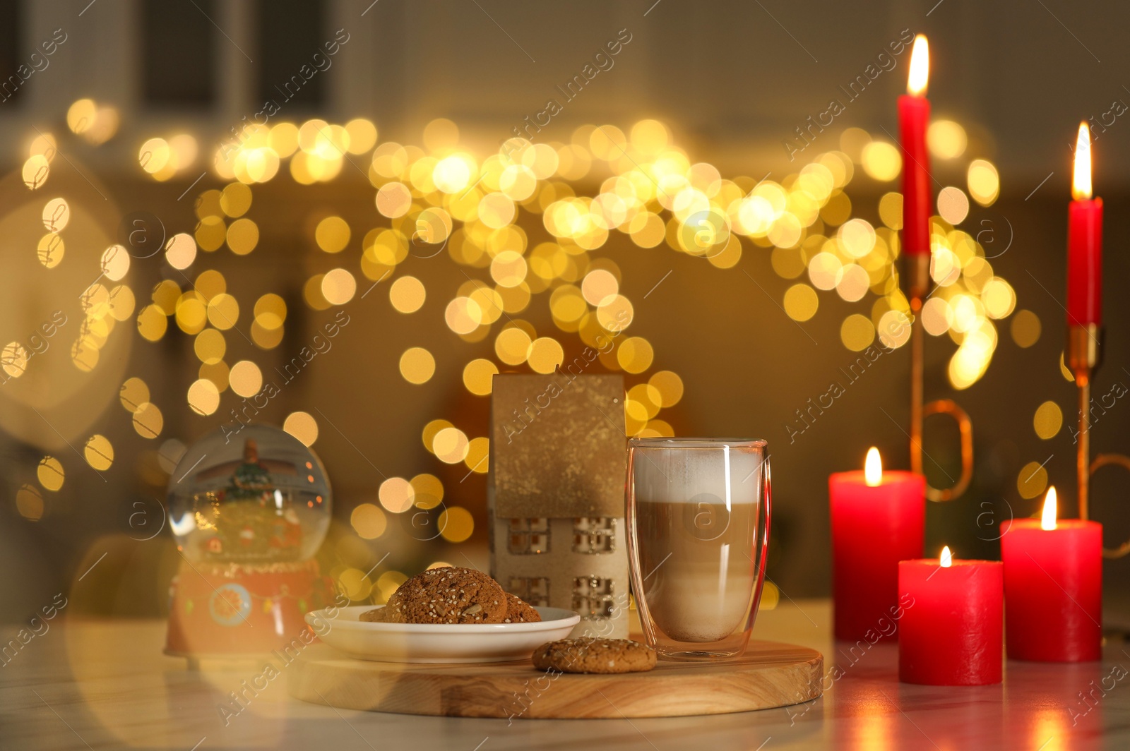 Photo of Aromatic coffee in glass, tasty cookies, Christmas decor and burning candles on table against blurred lights. Bokeh effect