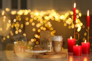 Photo of Aromatic coffee in glass, tasty cookies, Christmas decor and burning candles on table against blurred lights. Bokeh effect