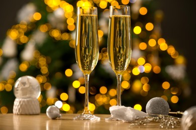 Photo of Champagne in glasses and decor on wooden table against blurred Christmas lights, bokeh effect